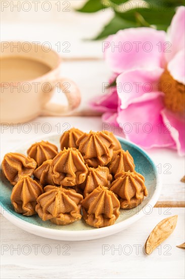 Homemade soft caramel fudge candies on blue plate and cup of coffee on gray concrete background, peony flower decoration. side view, close up, selective focus