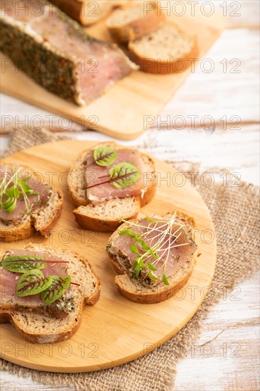 Bread sandwiches with jerky salted meat, sorrel and cilantro microgreen on white wooden background and linen textile. side view, close up, selective focus