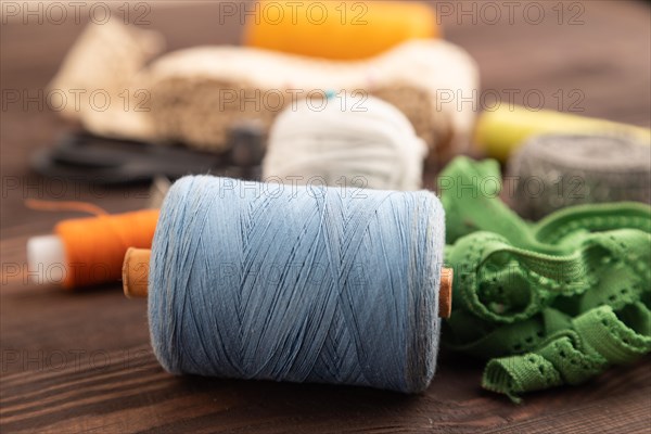 Sewing accessories: scissors, thread, thimbles, braid on brown wooden background. Side view, close up, selective focus
