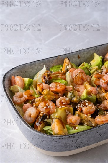 Closeup view of bowl with iceberg lettuce salad with shrimp, mussels and avocado