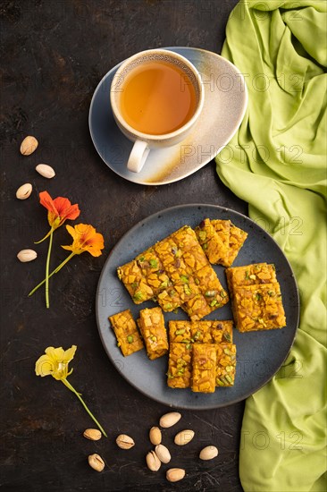 Traditional iranian dessert sohan with cup of green tea on a black concrete background and green textile. top view, flat lay, close up