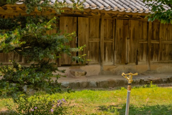 Copper water sprinkler in grassy lawn in front of wooden building located in public park displaying traditional Korean architecture