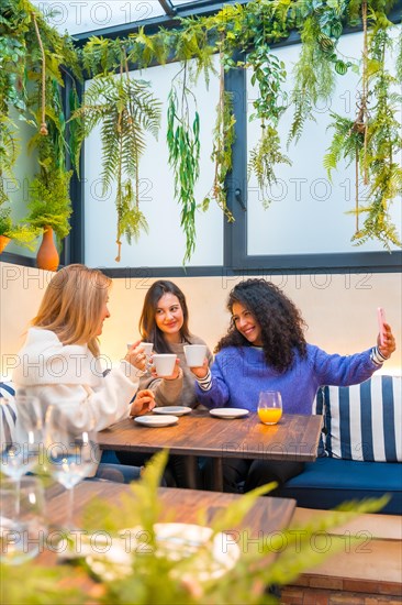 Vertical photo with copy space of three women taking selfie sitting together in a cafeteria