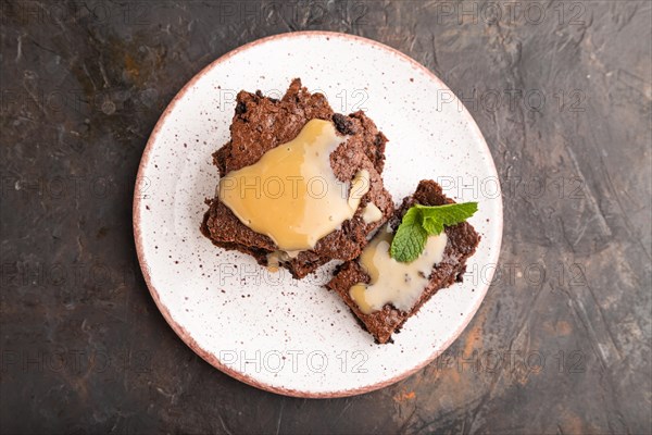 Chocolate brownie with caramel sauce with a cup of coffee on black concrete background. top view, flat lay, close up