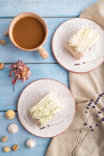 Roll biscuit cake with cream cheese and jam, cup of coffee on blue wooden background and linen textile. top view, flat lay, close up