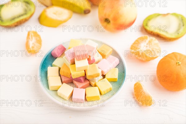 Various fruit jelly chewing candies on plate on white wooden background. apple, banana, tangerine, kiwi, side view, close up, selective focus