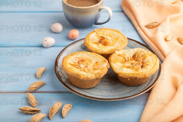 Traditional portuguese cakes pasteis de nata, custard small pies with almonds with cup of coffee on blue wooden background and orange textile. Side view, close up