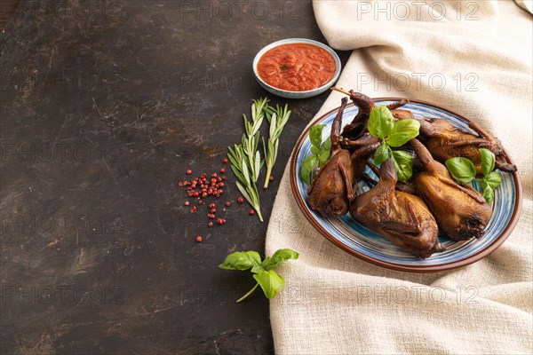 Smoked quail with herbs and spices on a ceramic plate with linen textile on a black concrete background. Side view, copy space