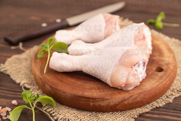 Raw chicken legs with herbs and spices on a wooden cutting board on a brown wooden background and linen textile. Side view, close up, selective focus