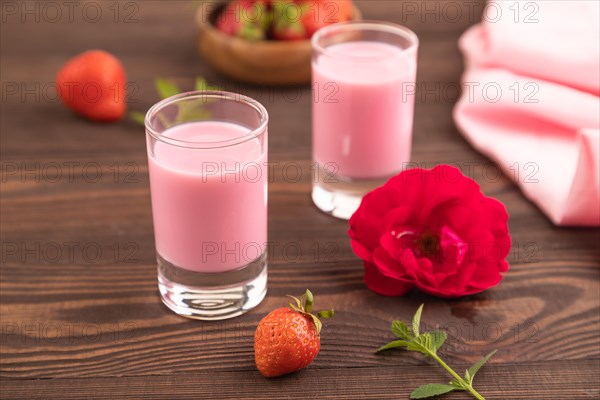 Sweet strawberry liqueur in glass on a brown wooden background and pink textile. side view, close up, selective focus