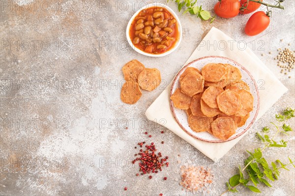 Slices of dehydrated salted meat chips with herbs and spices on gray concrete background and white textile. Top view, flat lay, copy space