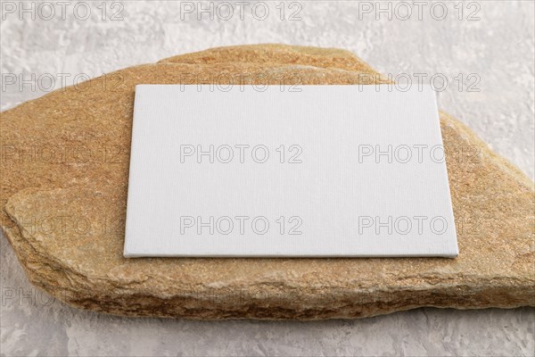 White paper business card, mockup with natural stone on gray concrete background. Blank, side view, still life, copy space, canvas