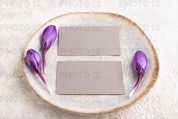 Gray paper invitation card, mockup with crocus flowers on ceramic plate and gray concrete background. Blank, flat lay, top view, still life, copy space, wedding invitation