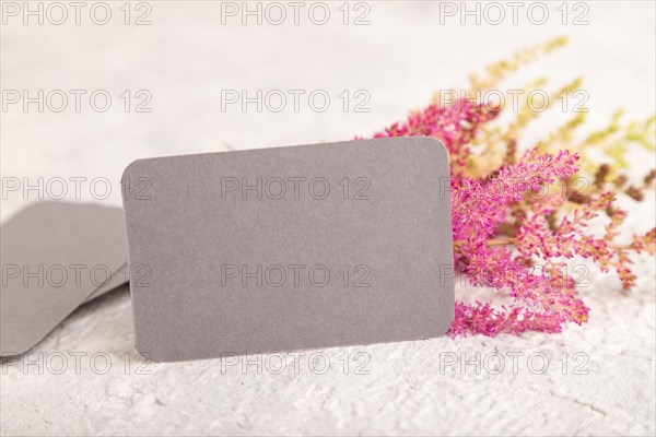 Gray paper business card mockup with purple astilbe flowers on gray concrete background. Blank, side view, copy space, still life. spring concept