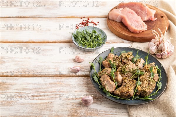Stewed turkey fillet with garlic and sprouts of green peas on white wooden background and linen textile. Side view, copy space