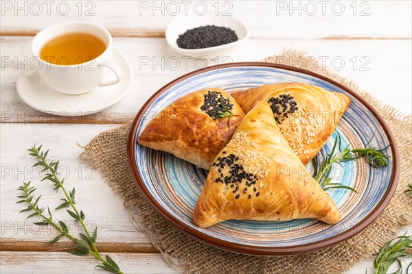 Homemade asian pastry samosa, cup of green tea on white wooden background and linen textile. side view