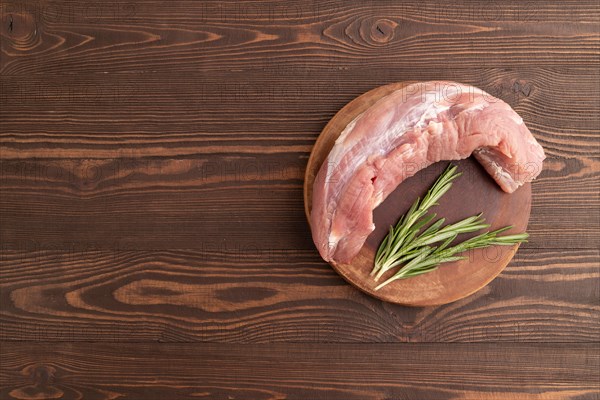 Raw pork with herbs and spices on a wooden cutting board on a brown wooden background. Top view, flat lay, copy space