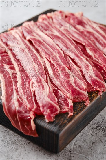 Closeup view of fresh raw beef bacon strips on wooden cutting board