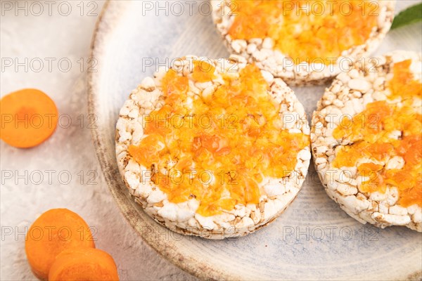 Carrot jam with puffed rice cakes on gray concrete background. Side view, close up, selective focus