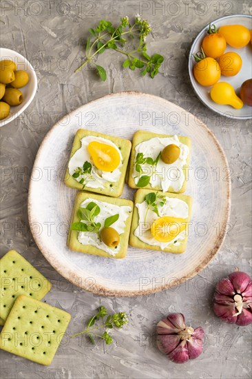 Green cracker sandwiches with cream cheese and cherry tomatoes on gray concrete background. top view, flat lay, close up