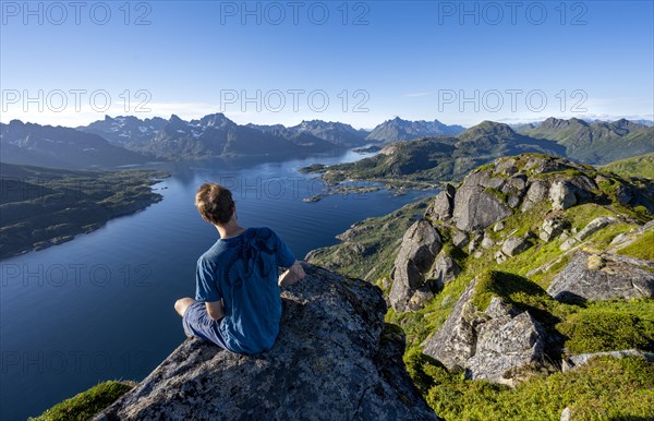 Mountaineer sitting on the summit of Dronningsvarden or Stortinden, behind mountains and fjord Raftsund, Sonnenstern, Vesteralen, Norway, Europe