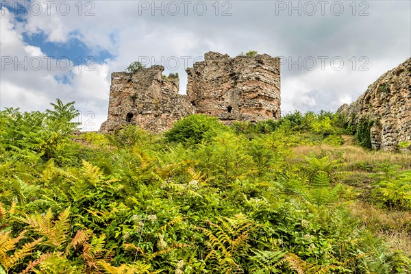 Remains of brick and stone castle towers on hillside under cloudy sky in Turkey