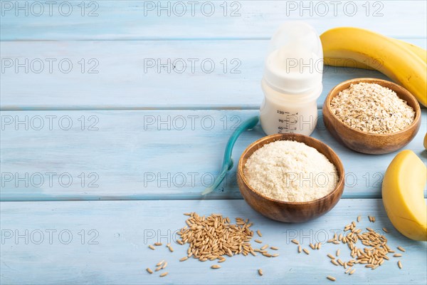 Powdered milk and oatmeal, banana baby food mix, infant formula, pacifier, bottle, spoon on blue wooden background. Side view, copy space, artificial feeding concept