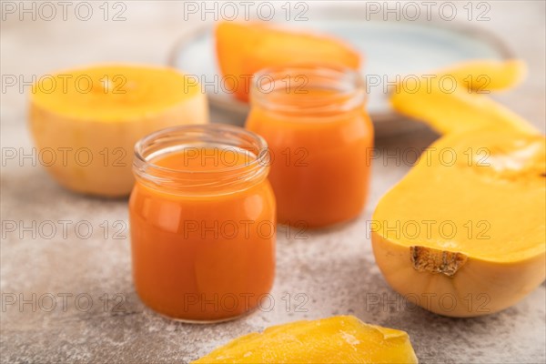 Baby puree with fruits mix, pumpkin, persimmon, mango infant formula in glass jar on brown concrete background. Side view, close up, selective focus, artificial feeding concept