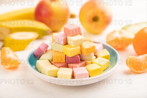 Various fruit jelly chewing candies on plate on white wooden background. apple, banana, tangerine, kiwi, side view, close up, selective focus