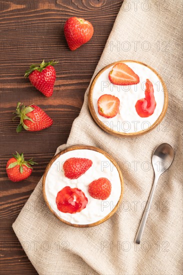 Grained cottage cheese with strawberry jam on brown wooden background and linen textile. top view, flat lay, close up