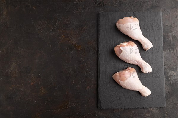 Raw chicken legs on a black slate cutting board on a black concrete background. Top view, flat lay, copy space