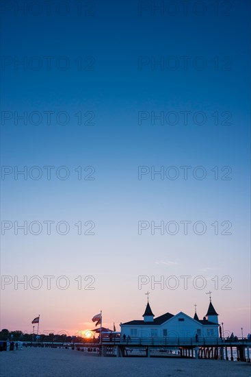 People strolling on a pier with buildings in the sunset, clear, blue, cloudless sky, pier Ahlbeck in the last sunlight, view from the eastern beach to the west, seaside resort Ahlbeck, island Usedom, Mecklenburg-Western Pomerania, Germany, Europe