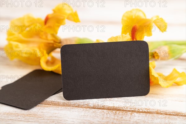 Black business card with iris yellow flowers on white wooden background. side view, copy space, mockup, template, spring, summer minimalism concept