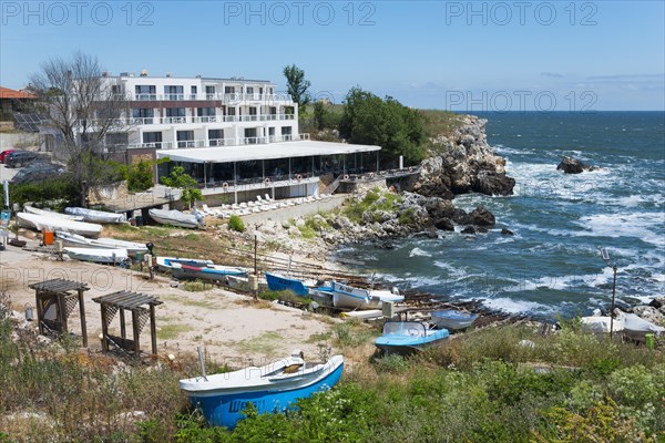 A hotel on the rocky coast with a view of the sea and several boats moored on the beach, harbour and hotel, Tyulenovo, Shabla, Dobrich, Black Sea, Bulgaria, Europe