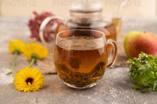 Red tea with herbs in glass teapot on brown concrete background and linen textile. Healthy drink concept. Side view, close up, selective focus