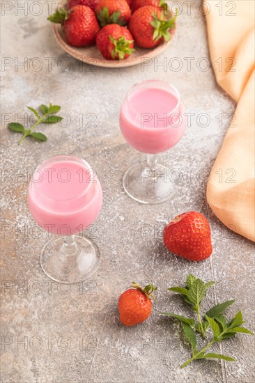 Sweet strawberry liqueur in glass on a gray concrete background and orange textile. side view, close up
