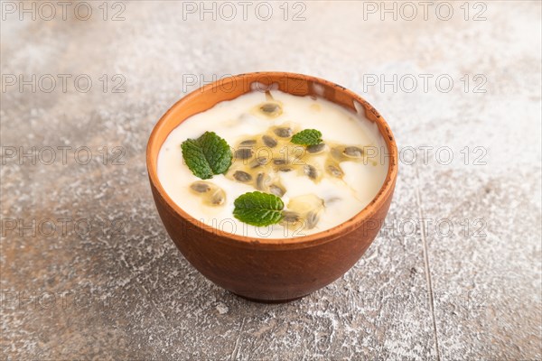 Yoghurt with granadilla and mint in clay bowl on brown concrete background. side view, close up