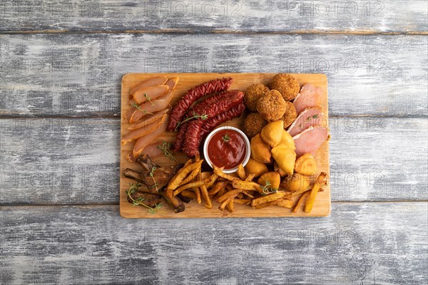Set of snacks: sausages, fried potatoes, meat balls, dumplings, basturma on a cutting board on a gray wooden background. Top view, flat lay, close up, copy space