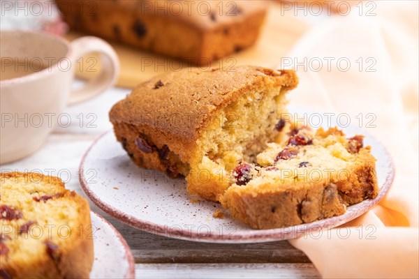 Homemade cake with raisins, almonds, soft caramel and a cup of coffee on a white wooden background and orange linen textile. Side view, close up, selective focus