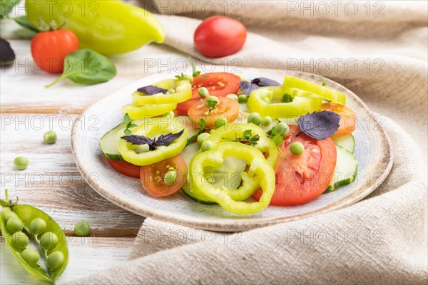 Vegetarian salad from green pea, tomatoes, pepper and basil on white wooden background and linen textile. Side view, close up