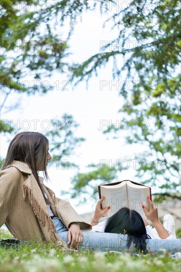 Side view of two relaxed female friends enjoying a day together in the park while getting some fresh air and reading a book