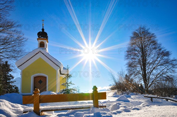Backlit photograph of the snow-covered Maria Chapel on the hummocky meadows of Werdenfelser Land near Garmisch in a wintry idyll, Bavaria, Germany, Europe