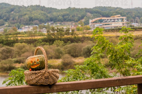 Jack-O-Lantern in wicker basket sitting on wooden railing with river and trees blurred out in background in South Korea