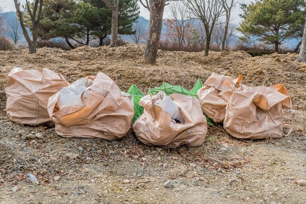 Burlap bags filled with trash on ground in front of trees at construction site