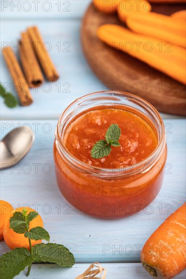 Carrot jam with cinnamon in glass jar on blue wooden background. Side view, close up, selective focus