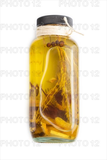 Sunflower oil in a glass jar with various herbs and spices, lavender, sesame, rosemary isolated on white background. Side view, copy space