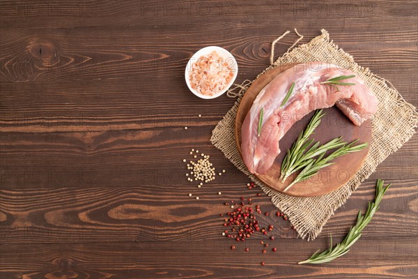 Raw pork with herbs and spices on a wooden cutting board on a brown wooden background. Top view, flat lay, copy space