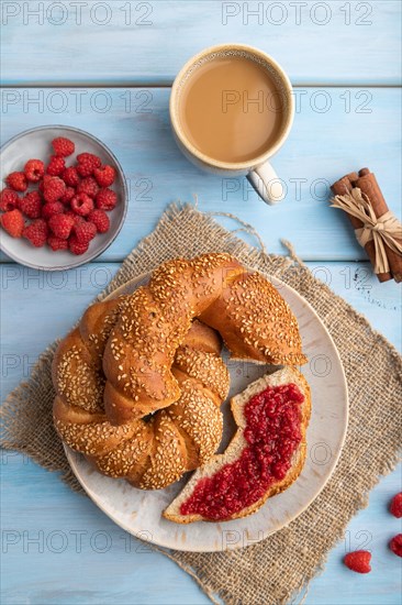 Homemade sweet bun with raspberry jam and cup of coffee on a blue wooden background and linen textile. top view, flat lay, close up