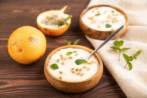 Yoghurt with granadilla and mint in wooden bowl on brown wooden background and linen textile. side view, close up, selective focus