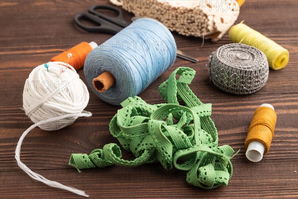 Sewing accessories: scissors, thread, thimbles, braid on brown wooden background. Side view, close up